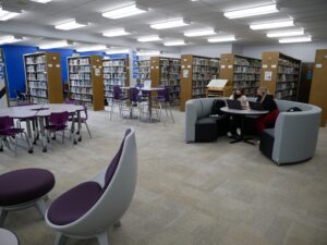 tables in chairs in grays and dark blues surrounded by books shelves